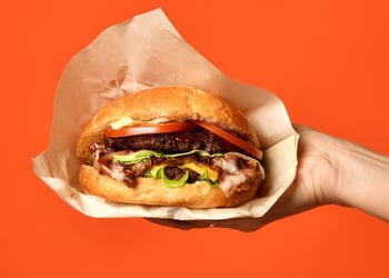 A hand holding a bacon cheeseburger with lots of toppings