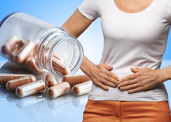 Person feeling their stomach while pills from a bottle come out in a background