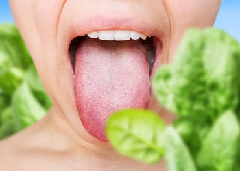 A person with their mouth wide open surrounded by spinach leaves