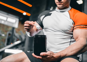 Person scooping a creatine supplement in a gym environment