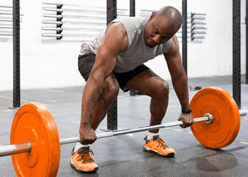 Dark skin person preparing to deadlift orange bar