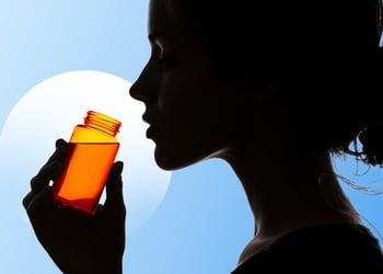 A silhouette of a person drinking an orange supplement shot