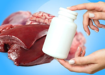 A hand holding a bottle supplements with organ meat in the background