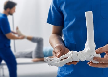 Podiatrist showing anatomical foot skeleton model during his assistant examination
