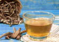 Transparent cup of valerian tea with valerian root on the side, set on a blue table