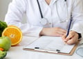 Female nutritionist writing diet plan on table with colorful fruits and vegetables